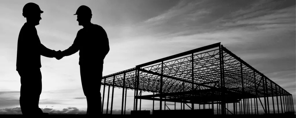 Dois empresários apertando as mãos em frente a uma construção moderna, representando parcerias no setor de construção nos EUA.